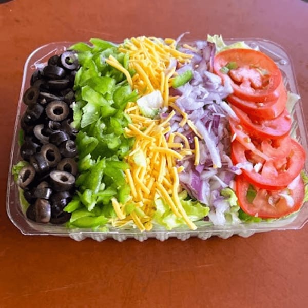 A plastic container of salad with sliced olives, green peppers, shredded cheese, red onions, and tomatoes.