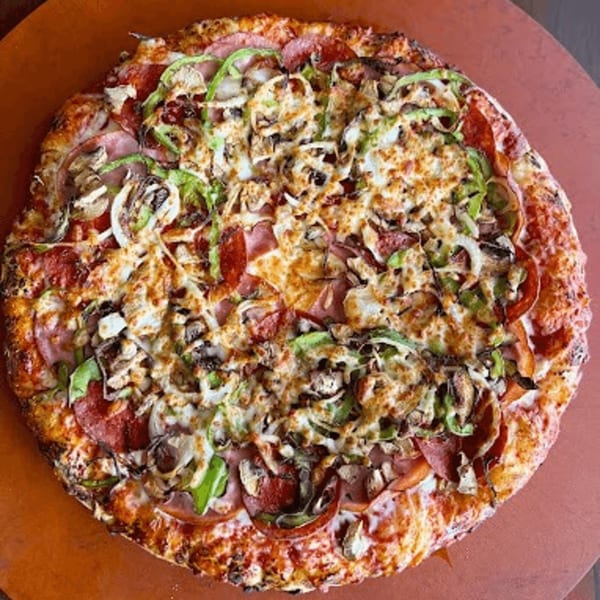A Detroit-style pizza with pepperoni, ham, green peppers, onions, and mushrooms on a red surface.