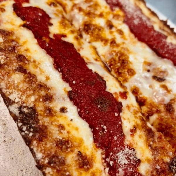 Close-up of Detroit-style pizza with thick red sauce stripes, melted cheese, and crispy crust.