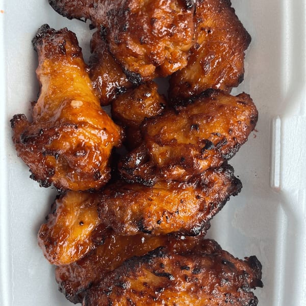 Close-up of several glazed and charred chicken wings in a white container from Detroit Pizza.