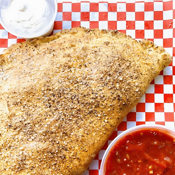 A golden-brown calzone sprinkled with herbs and cheese, served with marinara and white dipping sauces.