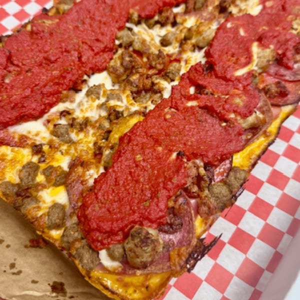 A close-up of a Detroit-style pizza with thick red sauce stripes, melted cheese, and sausage.